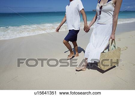 Low section of a couple holding hands and walking at beach View Large Photo Image Stock Image - Low section of a couple holding hands and walking at beach. Fotosearch