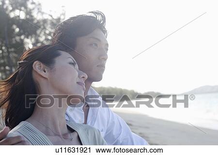 Stock Image - Profile of a young couple sitting on beach. Fotosearch