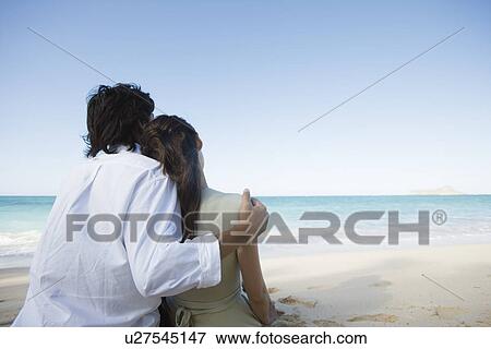 Stock Photo - Rear view of a couple sitting on beach. Fotosearch