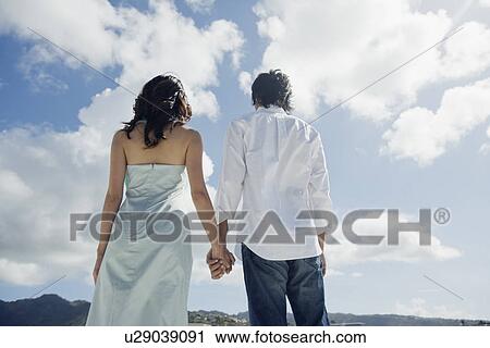 Rear view of a young couple holding hands View Large Photo Image Stock Image - Rear view of a young couple holding hands. Fotosearch