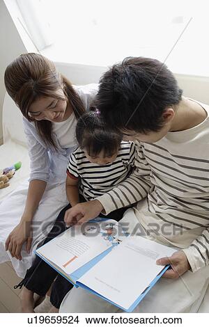 Picture - A young couple reading a book to their child. Fotosearch