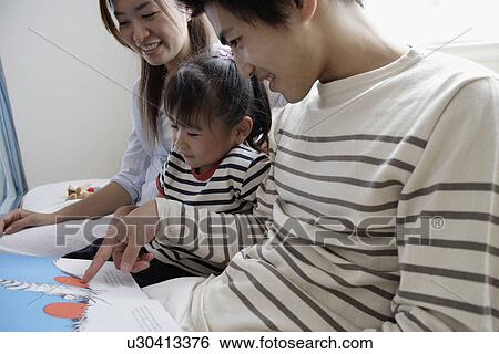 Stock Photograph - A young couple reading a book to their child. Fotosearch