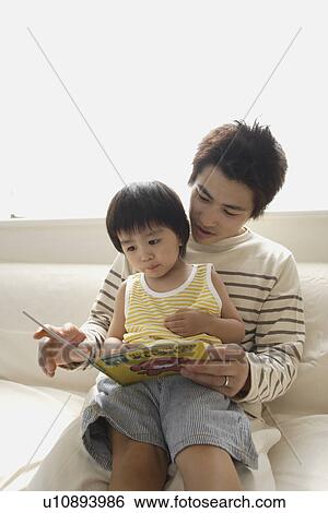 Stock Photograph - A young father reading a book to his son. Fotosearch