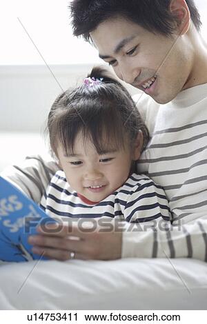 Stock Image - A young father reading a book to his daughter. Fotosearch