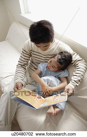 Stock Image - A young father reading a book to his daughter. Fotosearch