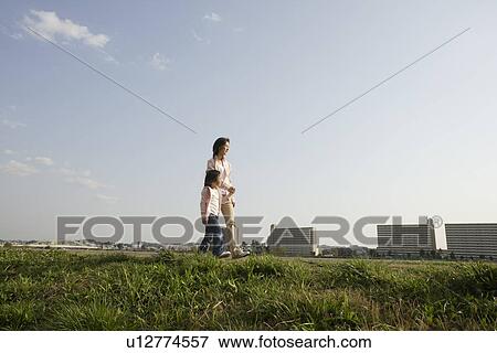 Stock Photo - Side view of a mother and daughter walking on grass. Fotosearch