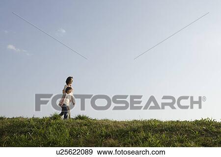 Stock Photo - Side view of a mother and daughter walking on grass. Fotosearch