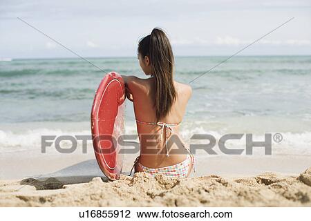 Stock Image - Rear view of a young woman sitting on beach. Fotosearch