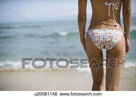 Stock Photo - Rear view of a young woman standing on beach. Fotosearch
