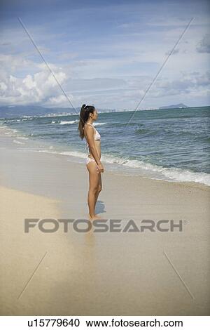 View of a young woman standing on beach View Large Photo Image Stock Image - View of a young woman standing on beach. Fotosearch