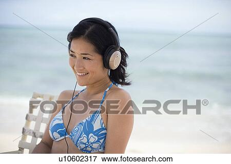 Stock Photo - A woman listening to music at beach. Fotosearch