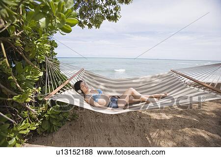 Stock Photo - A woman lying on hammock at beach. Fotosearch
