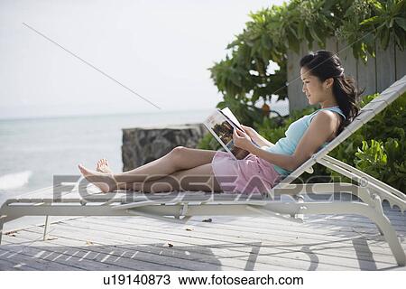 Stock Image - A woman reading book on deck chair. Fotosearch