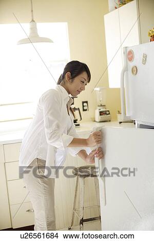 Picture - A young woman opening refrigerator in kitchen. Fotosearch