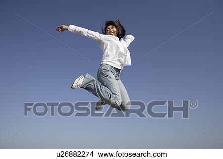 Picture - Low angle view of a smiling young woman jumping in air. Fotosearch