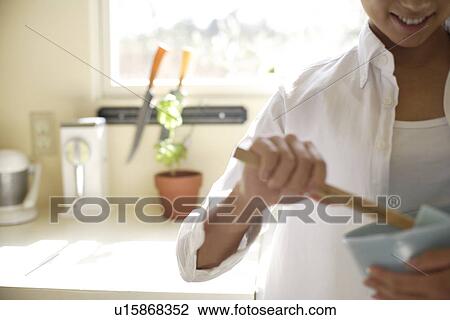 Stock Image - Midsection of a young woman holding spatula and bowl. Fotosearch