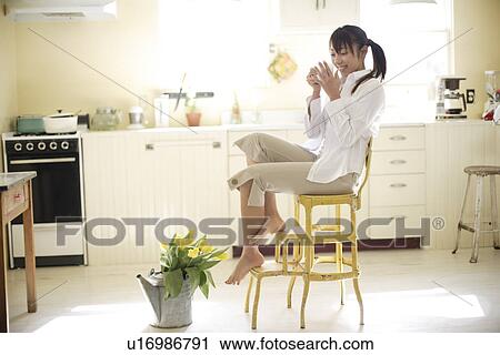 Stock Image - View of a woman sitting on chair in kitchen. Fotosearch