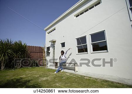 Stock Image - View of a young woman sitting on the bench in garden. Fotosearch