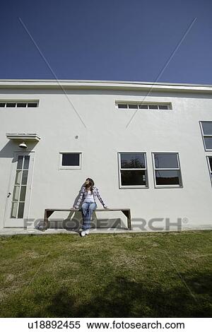 View of a young woman sitting on the bench outside house View Large Photo Image Stock Photography - View of a young woman sitting on the bench outside house. Fotosearch