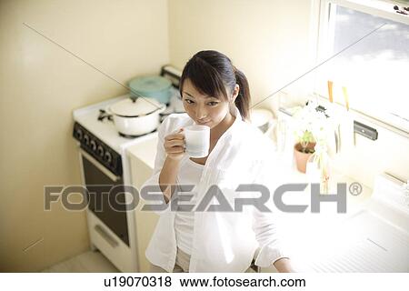 Young woman drinking cup of coffee in kitchen View Large Photo Image Stock Photo - Young woman drinking cup of coffee in kitchen. Fotosearch