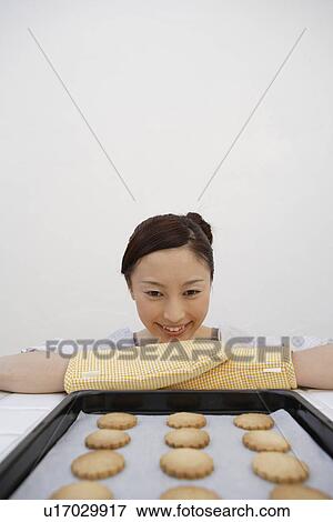 A smiling young woman looking at the tray of biscuits View Large Photo Image Stock Photo - A smiling young woman looking at the tray of biscuits. Fotosearch