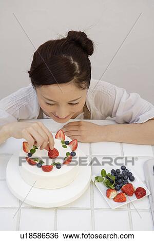 Stock Photograph - Elevated view of a young woman garnishing a pastry. Fotosearch