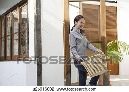 Stock Image - Side view of a young woman carrying a basket. Fotosearch
