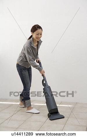 Stock Photo - Side view of a young woman cleaning floor with a vacuum cleaner. Fotosearch