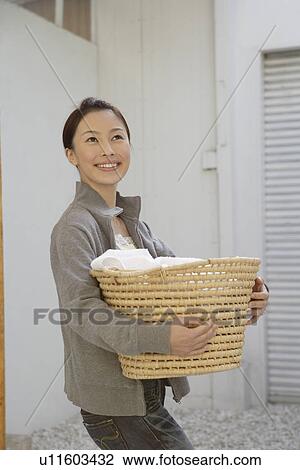 Stock Image - Side view of a young woman holding a basket. Fotosearch