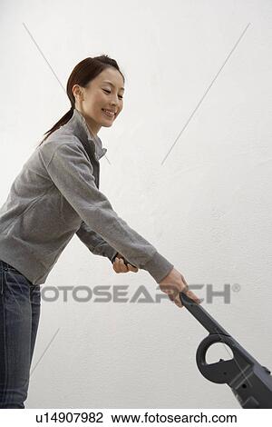 Side view of a young woman using a vacuum cleaner View Large Photo Image Stock Image - Side view of a young woman using a vacuum cleaner. Fotosearch