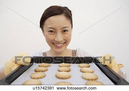 Stock Image - View of a young woman holding a tray of biscuits. Fotosearch