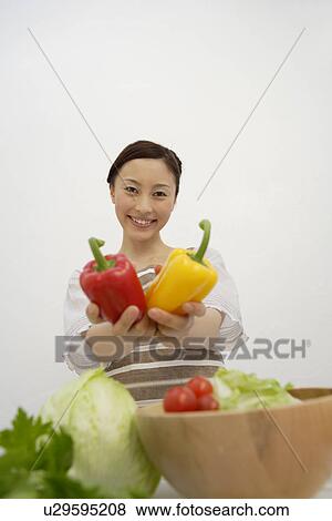 Stock Photo - View of a young woman holding bell peppers in her hands. Fotosearch