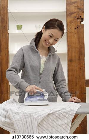 Stock Photography - View of a young woman ironing a shirt. Fotosearch