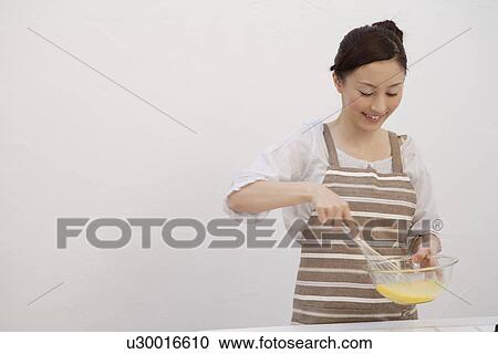 Stock Image - View of a young woman mixing egg yolk with whisk. Fotosearch