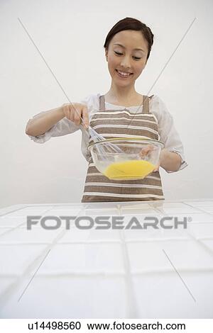 Stock Image - View of a young woman mixing egg yolks with whisk. Fotosearch