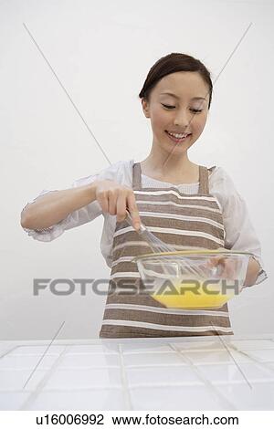 Stock Image - View of a young woman mixing eggs yolks with whisk. Fotosearch