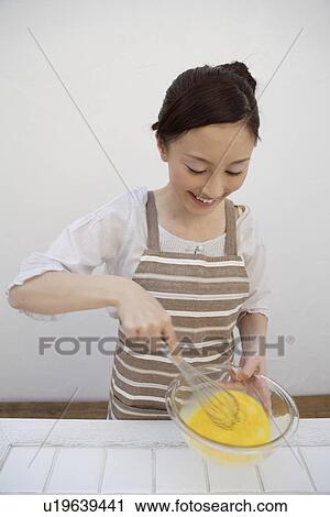 Stock Image - View of a young woman mixing eggs yolks with whisk. Fotosearch