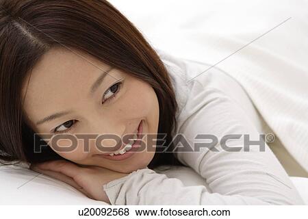 Stock Photo - A young woman lying on a bed. Fotosearch