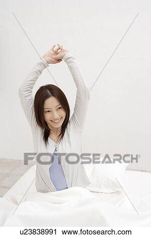 A young woman sitting on a bed View Large Photo Image Stock Image - A young woman sitting on a bed. Fotosearch