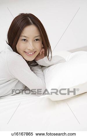 Stock Photography - Side view of a cheerful woman lying on the bed. Fotosearch