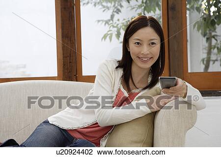 Stock Image - View of a young woman holding a remote control. Fotosearch