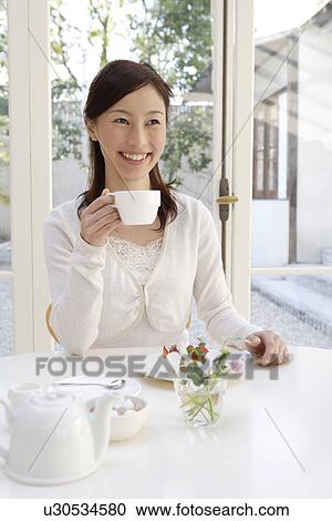 Stock Image - View of a young woman holding a teacup. Fotosearch