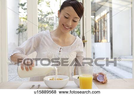 Stock Photo - View of a young woman pouring milk in a bowl. Fotosearch