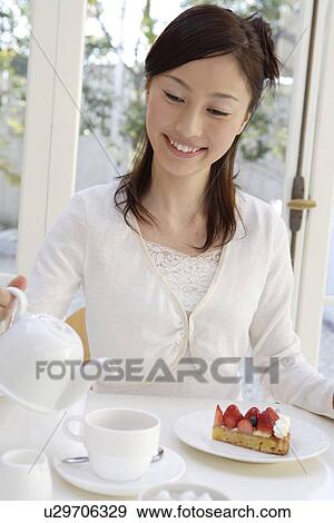 Stock Photo - View of a young woman pouring tea in a teacup. Fotosearch
