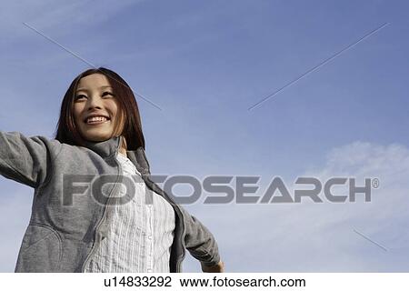 Stock Image - Low angle view of a woman standing with her arms stretched. Fotosearch
