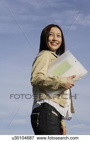 View of a young woman standing with a folder in her hand View Large Photo Image Stock Photo - View of a young woman standing with a folder in her hand. Fotosearch