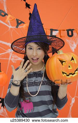 Stock Image - Portrait of teenage girl holding jack-o-lantern. Fotosearch