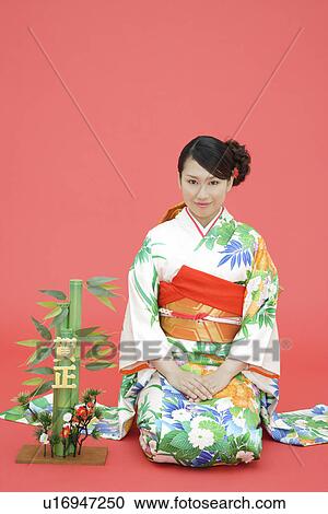 Stock Image - View of teenage girl in traditional outfit beside a plant. Fotosearch