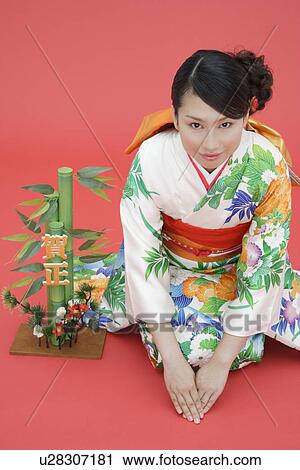 Stock Image - View of teenage girl in traditional outfit beside a plant. Fotosearch