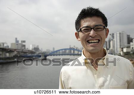 Stock Image - A smiling young man standing with river in background. Fotosearch
